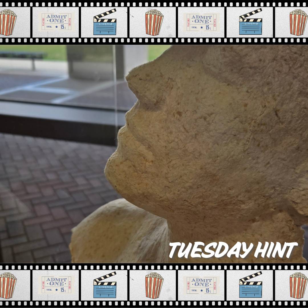 What looks to be a paper mache mask of a face inside a glass display with bricks in the background